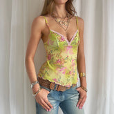 Woman wearing a floral tank top and jeans with jewelry against a neutral background